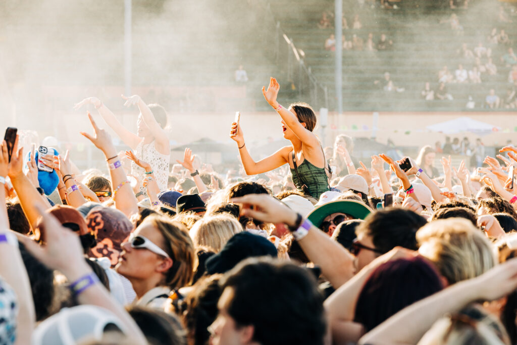 Girl with arms up on someone's shoulders in a busy music festival crowd.